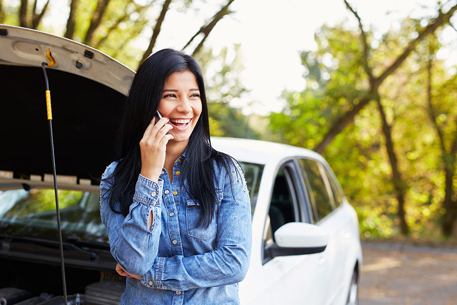 Client Center - Portrait of a Cheerful Young Woman Making a Phone Call While Standing Next to Her Car with the Front Hood Open on a Road Trip